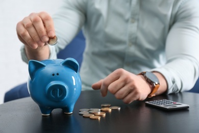 Photo of Businessman putting coin into piggy bank at table against light background, closeup. Money saving