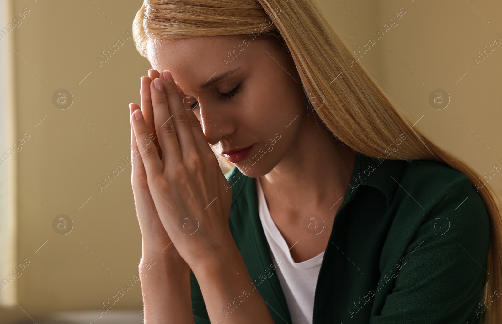 Photo of Religious young woman with clasped hands praying indoors