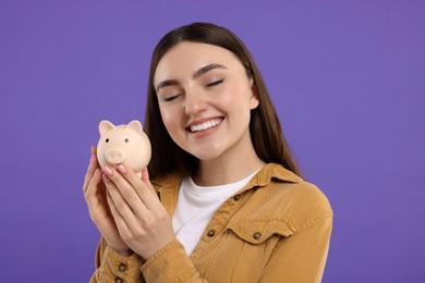 Photo of Happy woman with piggy bank on purple background