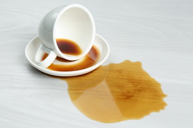 Overturned cup and spilled coffee on white wooden table