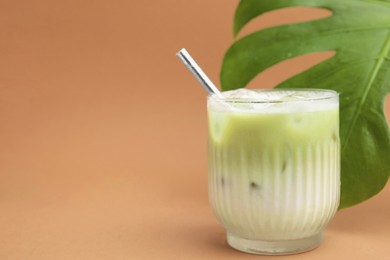 Photo of Glass of tasty iced matcha latte and leaf on light brown background. Space for text