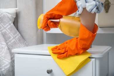 Woman cleaning white bedside table with detergent and rag indoors, closeup