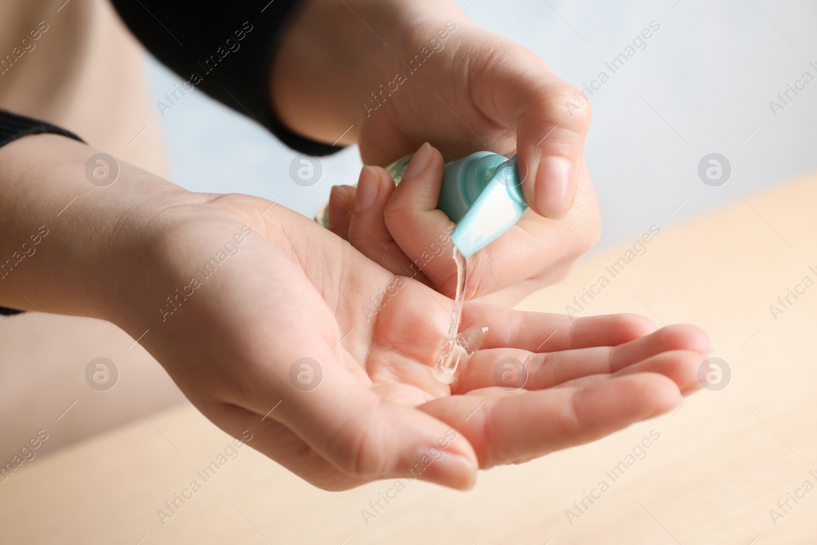 Photo of Woman applying antiseptic gel on hand against blurred background, closeup
