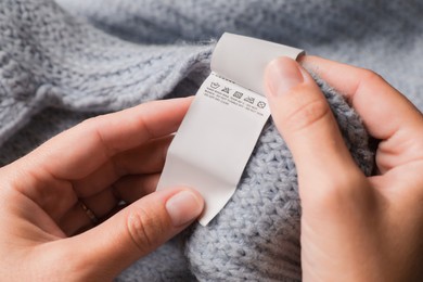 Photo of Woman holding clothing label on light blue garment, closeup