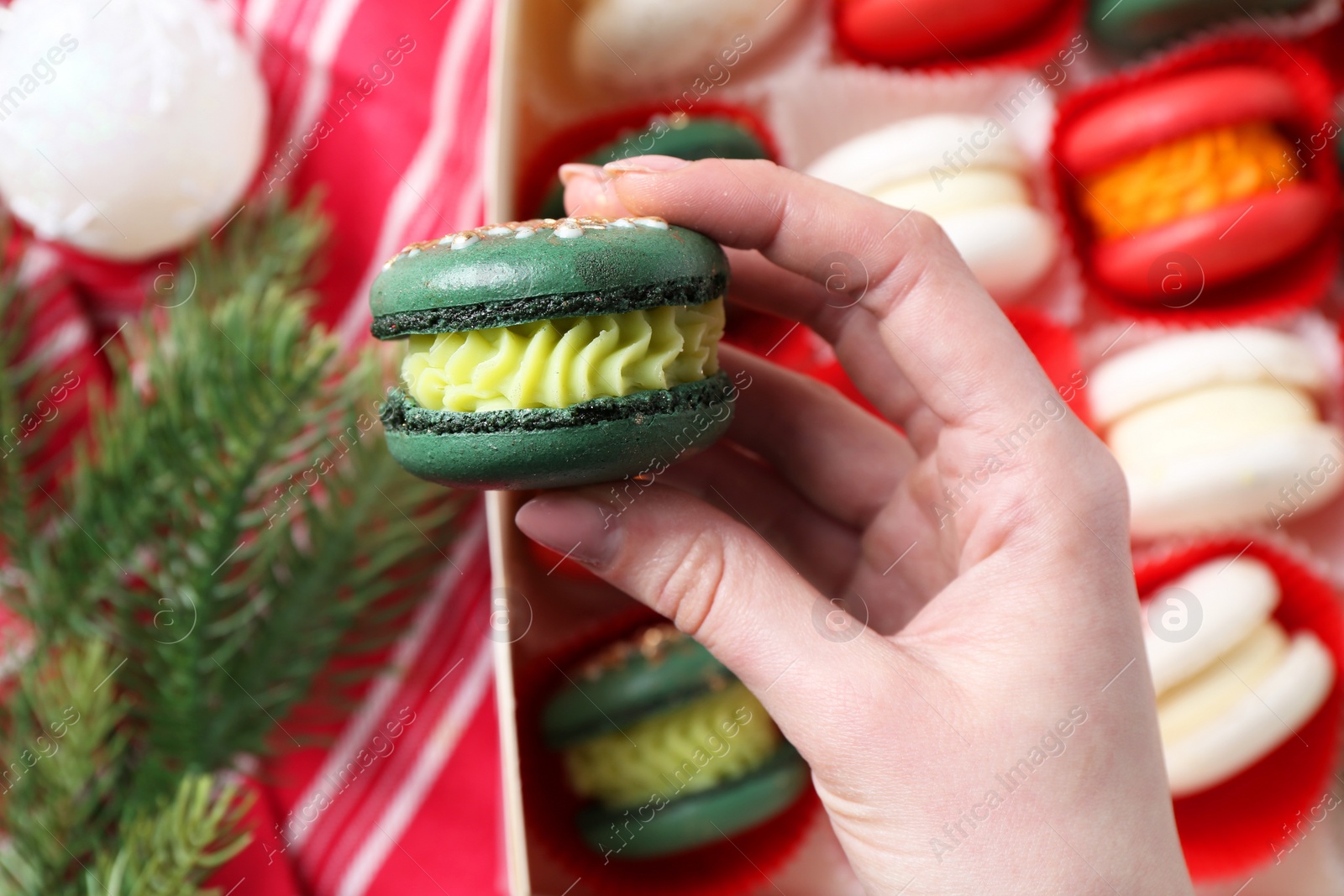 Photo of Woman with decorated Christmas macaron at table, closeup