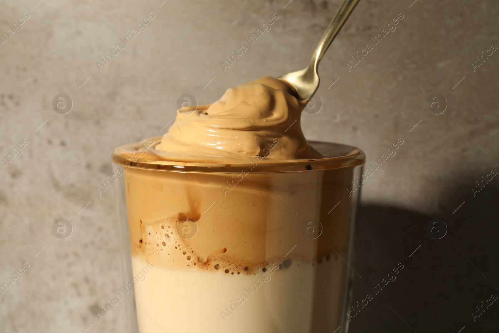 Photo of Putting cream for dalgona coffee into glass against grey wall, closeup