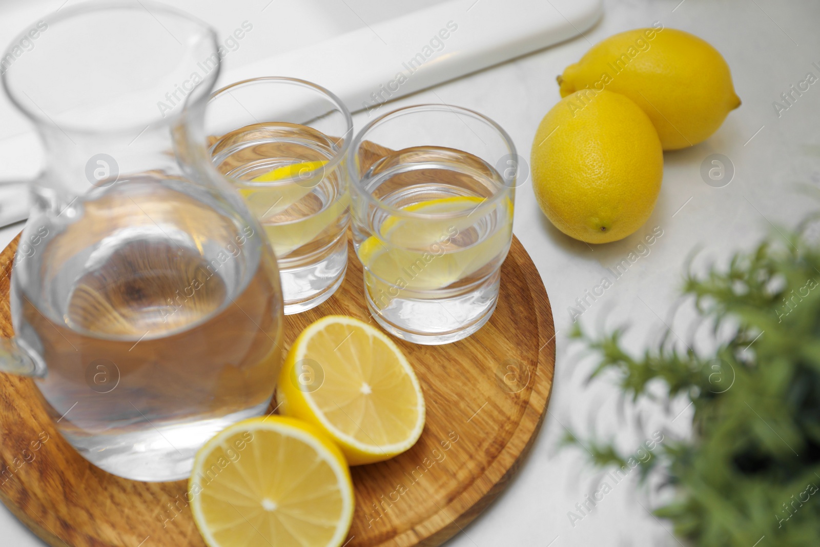 Photo of Jug, glasses with clear water and lemons on white table in kitchen, closeup