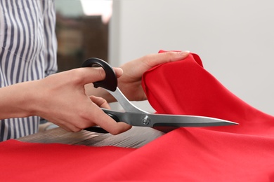 Woman cutting fabric with sharp scissors at wooden table indoors, closeup