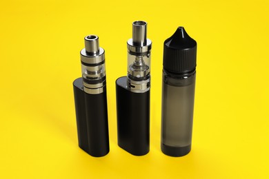 Photo of New reusable electronic cigarettes and vaping liquid on yellow background