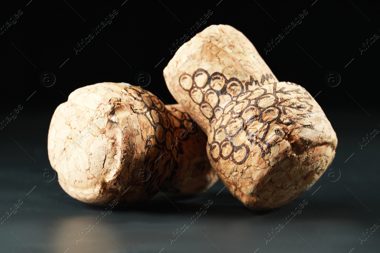 Photo of Corks of wine bottles with grape images on black table, closeup