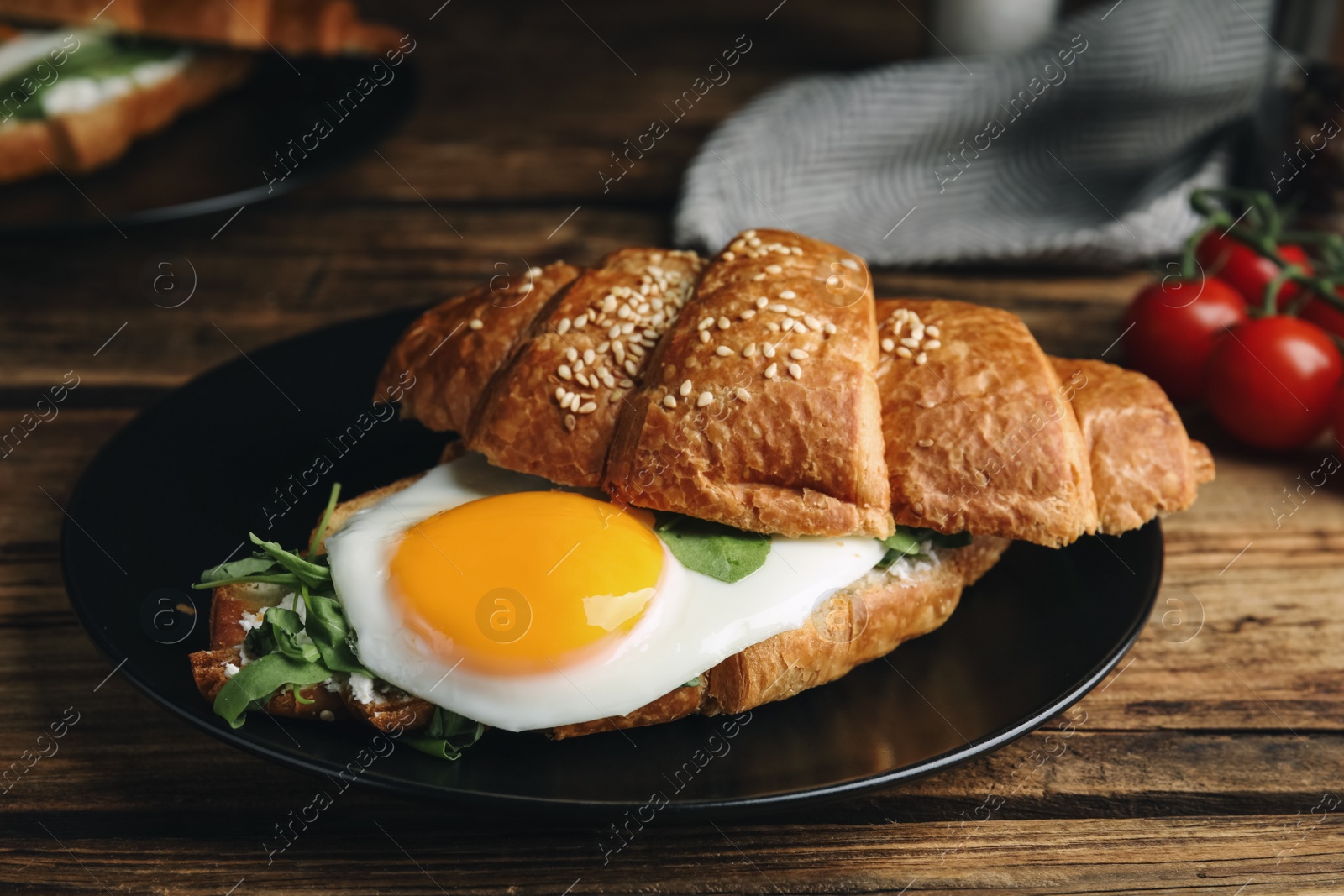 Photo of Delicious croissant with arugula and fried egg on wooden table, closeup