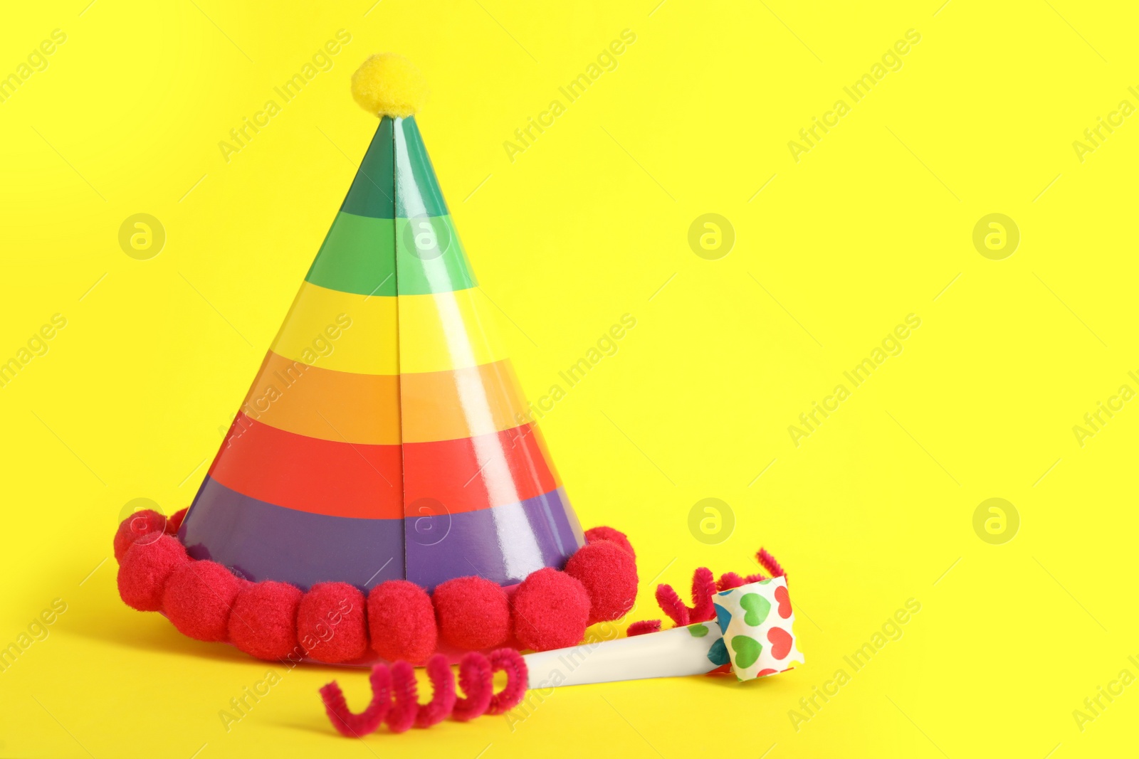 Photo of Party cap, blower and fluffy wires on yellow background, space for text