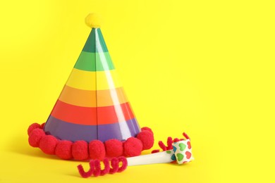 Party cap, blower and fluffy wires on yellow background, space for text