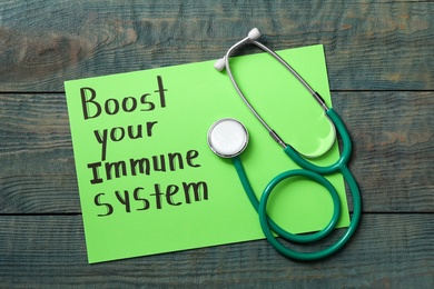 Photo of Paper sheet with text Boost your Immune System and stethoscope on blue wooden table, top view