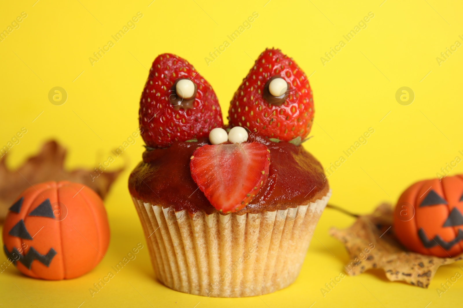 Photo of Delicious cupcake decorated as monster on yellow background. Halloween treat