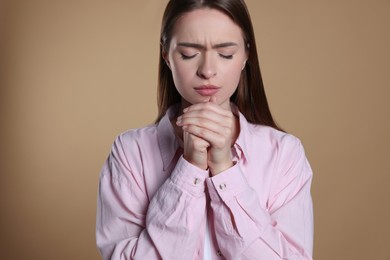 Woman with clasped hands praying on beige background