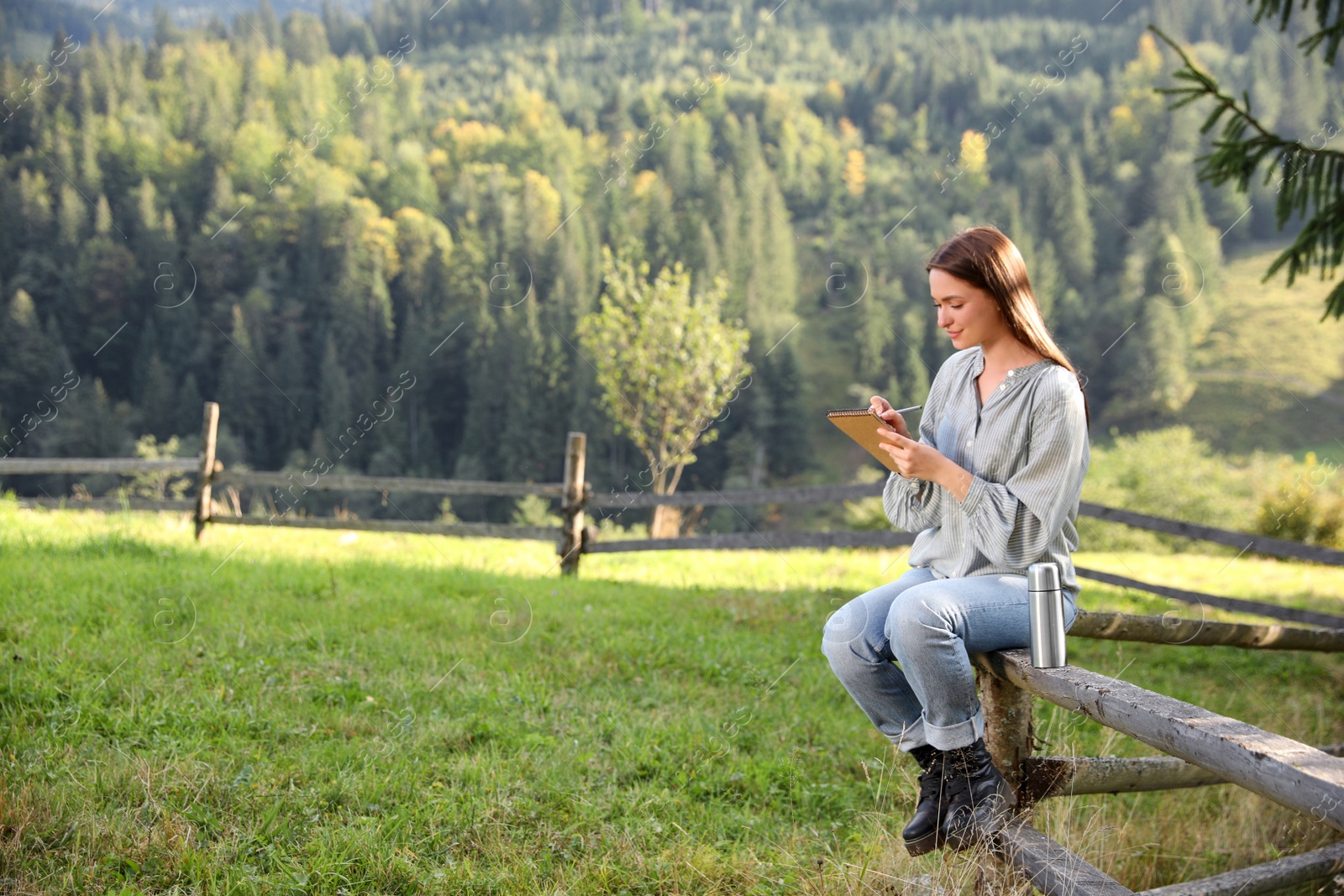 Photo of Beautiful young woman drawing with pencil in notepad on fence outdoors