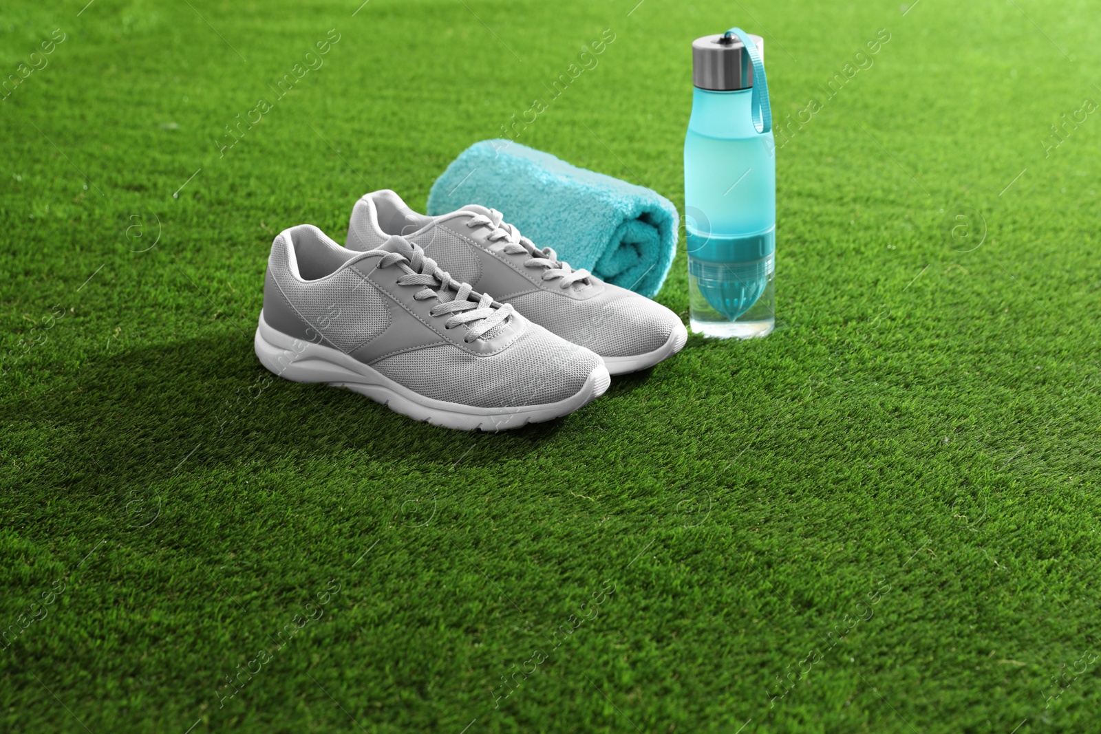 Photo of Bottle of water, sneakers, towel and space for text on artificial grass. Fitness equipment