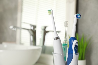 Photo of Electric toothbrushes in glass holder indoors, closeup. Space for text