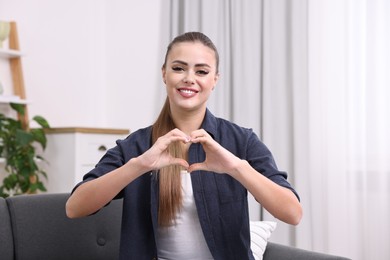 Photo of Happy woman showing heart gesture with hands at home