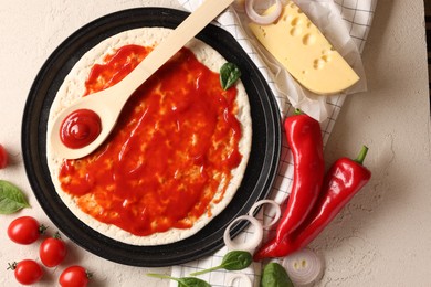 Pizza base smeared with tomato sauce and products on light textured table, flat lay