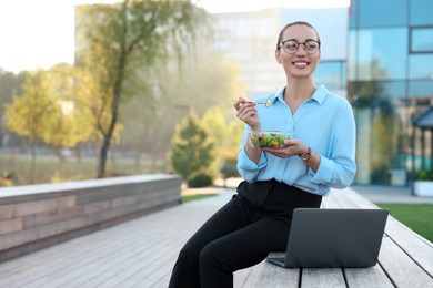 Photo of Smiling businesswoman with lunch box sitting near laptop outdoors. Space for text