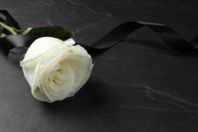 Photo of White rose and ribbon on black table, closeup with space for text. Funeral symbols