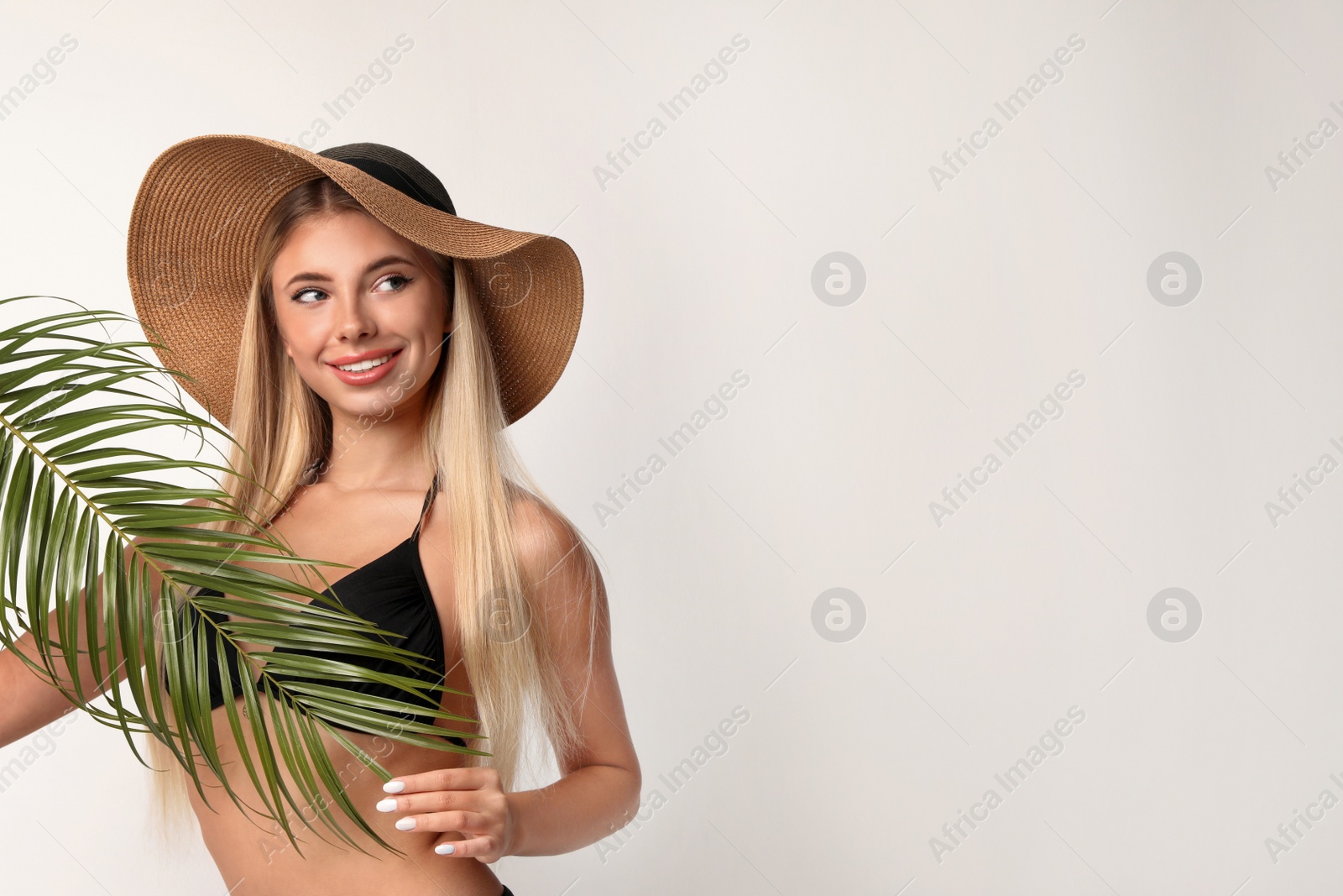 Photo of Pretty young woman wearing stylish bikini with palm leaf on light background. Space for text