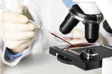 Photo of Scientist dripping blood sample onto slide on microscope in laboratory, closeup. Virus research