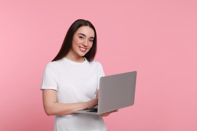 Photo of Smiling young woman working with laptop on pink background, space for text