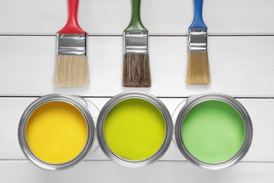 Cans of yellow and green paints with brushes on white wooden table, flat lay