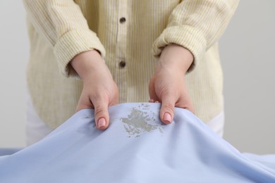Photo of Woman holding shirt with stain against light background, closeup