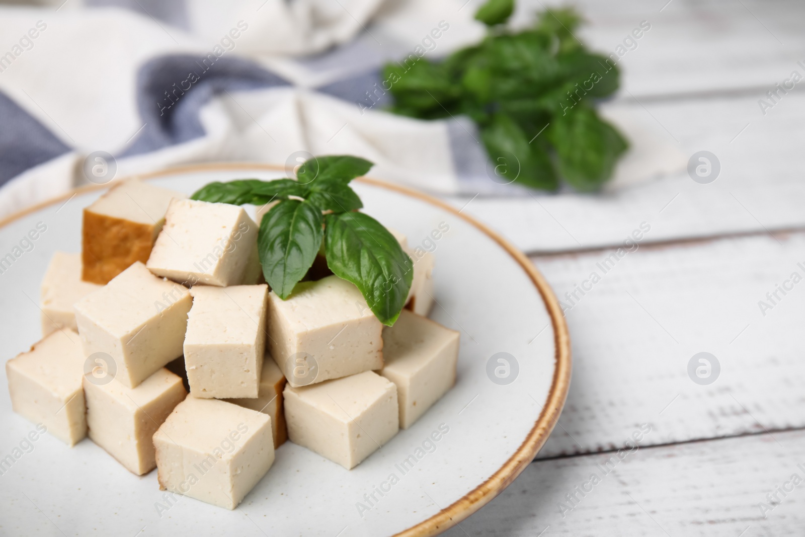 Photo of Plate with delicious smoked tofu and basil on white wooden table, closeup