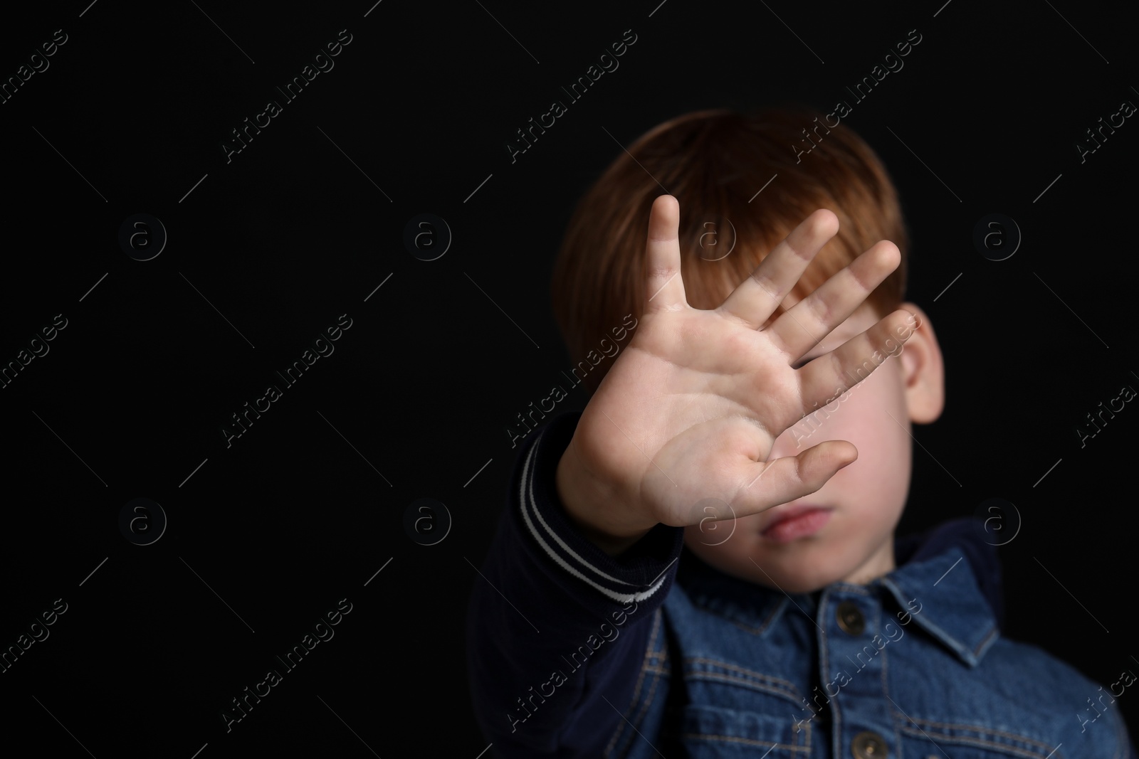 Photo of Boy making stop gesture against black background, focus on hand and space for text. Children's bullying