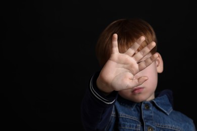 Photo of Boy making stop gesture against black background, focus on hand and space for text. Children's bullying