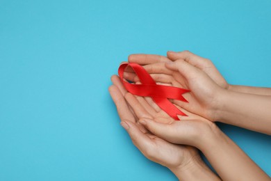 Photo of Woman and girl holding red ribbon on blue background, top view with space for text. AIDS disease awareness