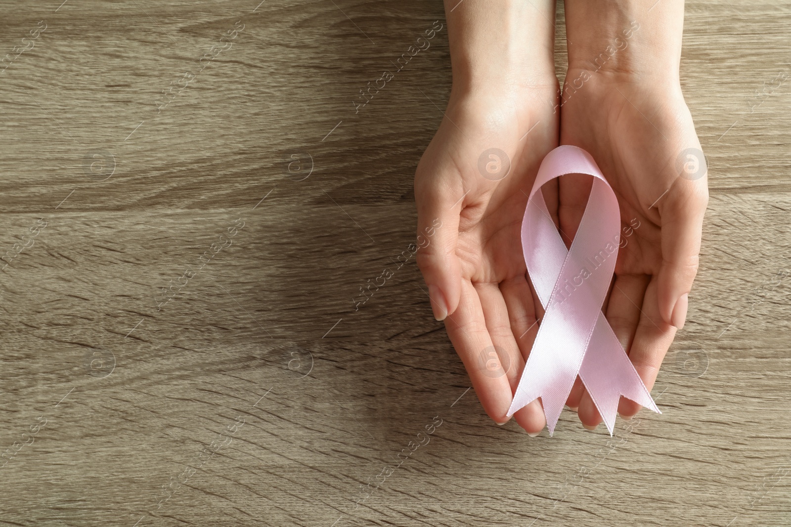 Photo of Woman holding pink ribbon on wooden background, top view with space for text. Breast cancer awareness