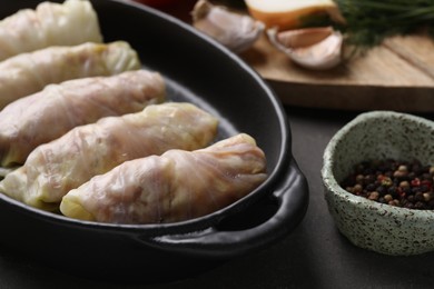 Photo of Uncooked stuffed cabbage rolls and spices on grey table, closeup