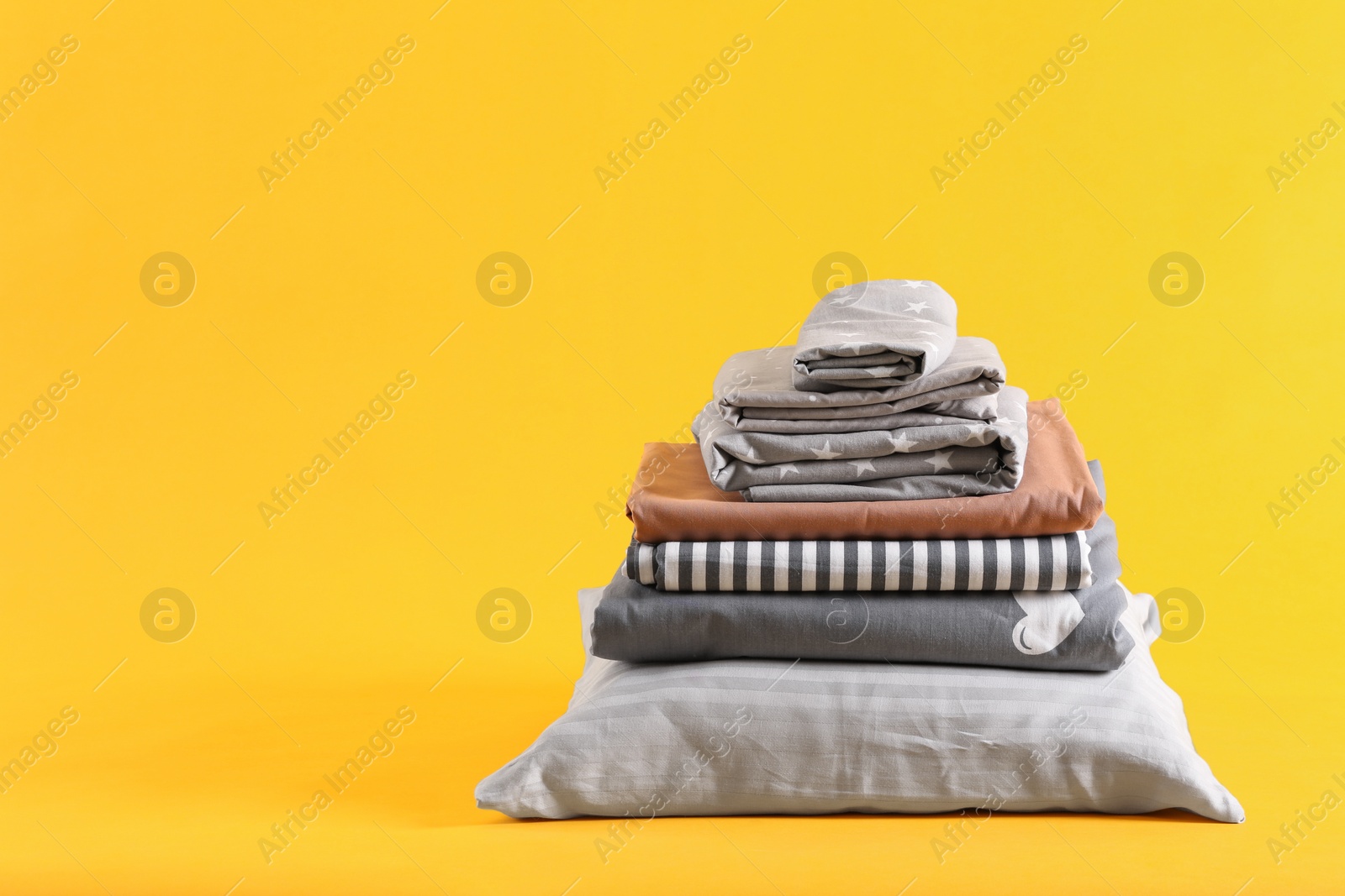 Photo of Stack of clean bed sheets and pillow on yellow background. Space for text