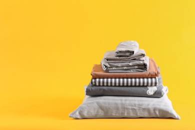 Stack of clean bed sheets and pillow on yellow background. Space for text