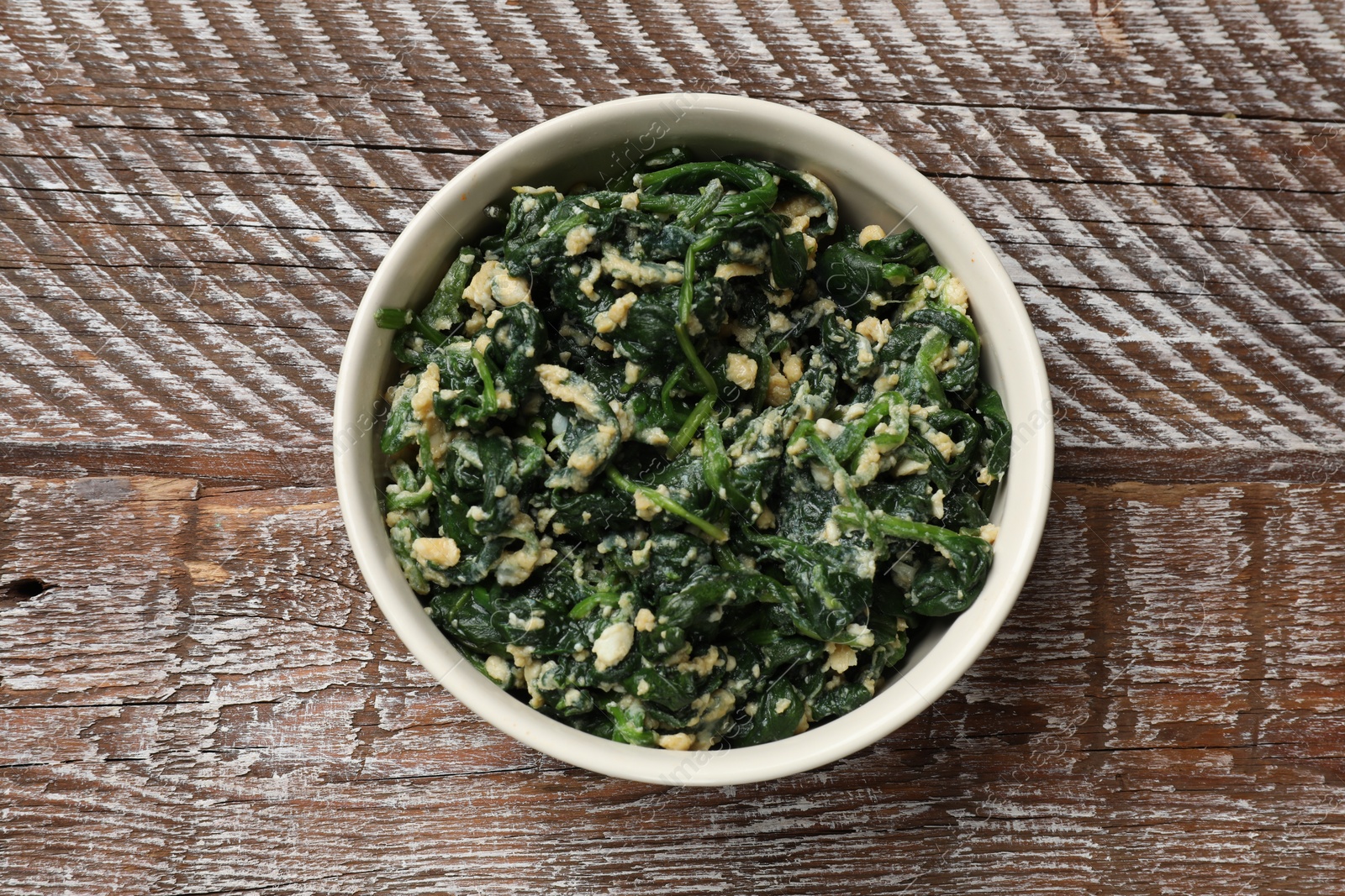 Photo of Tasty spinach dip with eggs in bowl on wooden table, top view