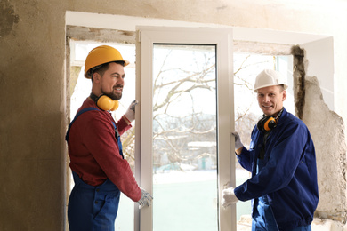 Workers in uniform installing plastic window indoors