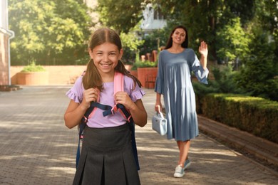 Mother waving goodbye to her daughter before school outdoors