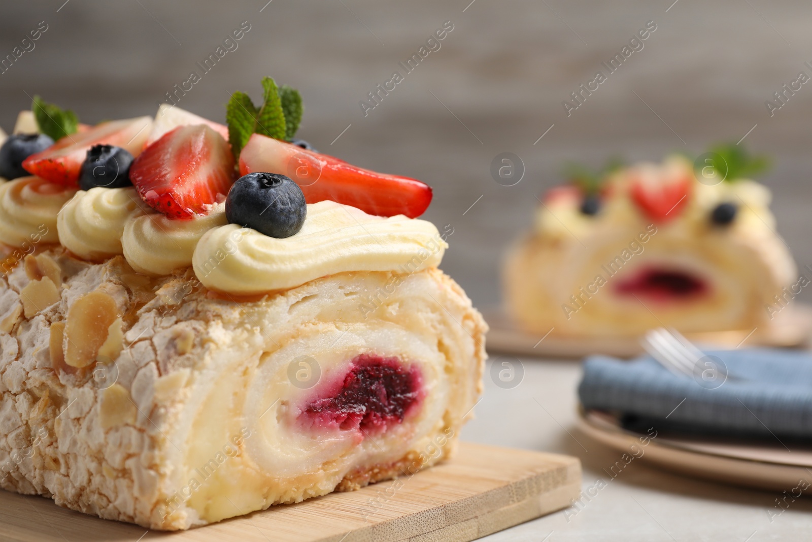 Photo of Tasty meringue roll with jam, cream, strawberry, blueberry and mint on light table, closeup. Space for text