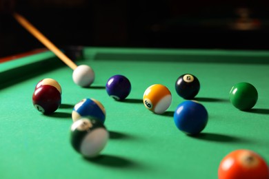 Many colorful billiard balls and cue on green table indoors