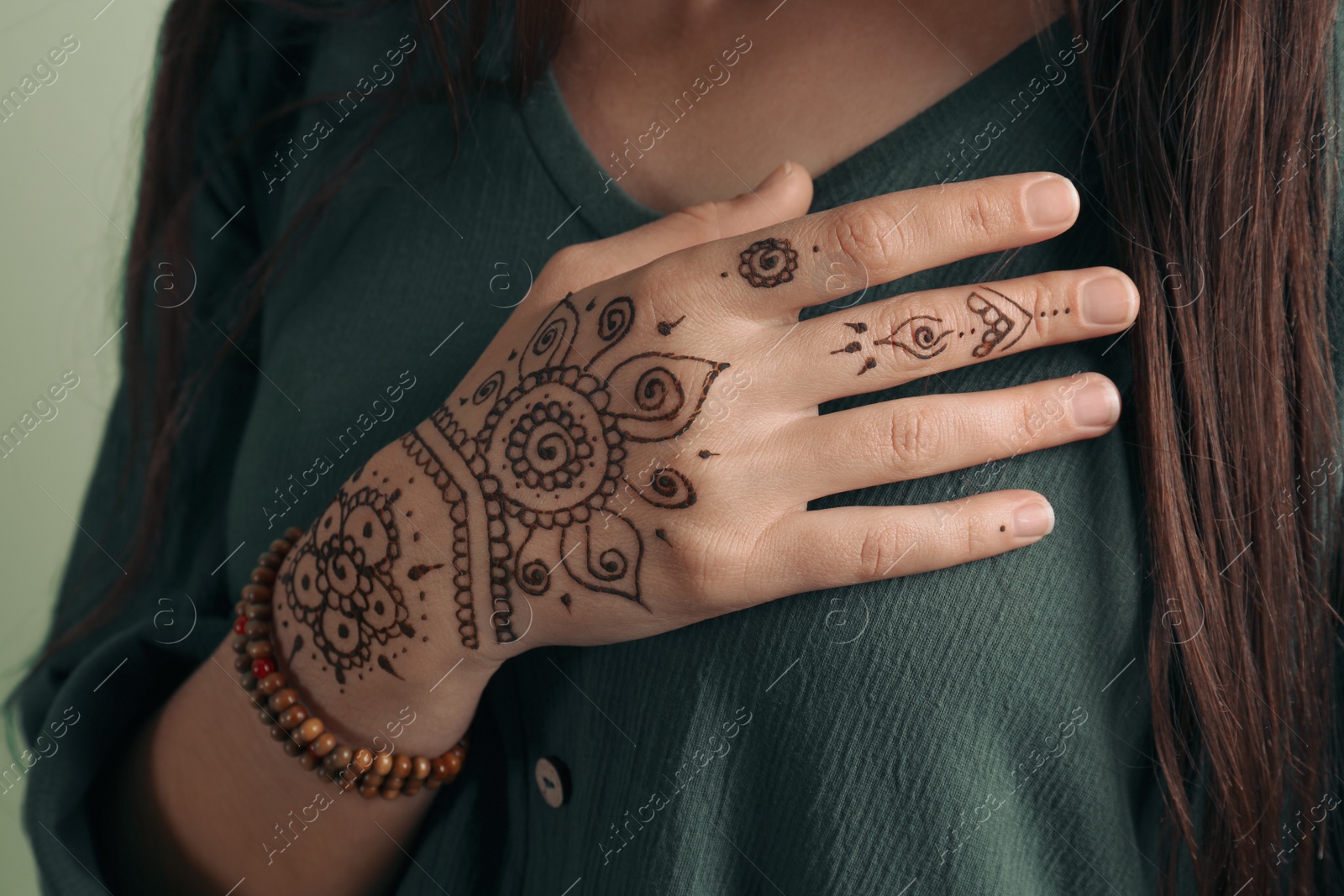 Photo of Woman with beautiful henna tattoo on hand against green background, closeup. Traditional mehndi