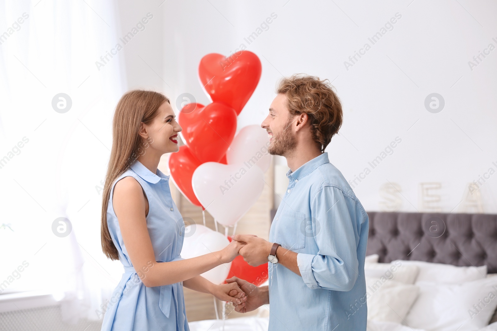 Photo of Young couple with air balloons in bedroom. Celebration of Saint Valentine's Day