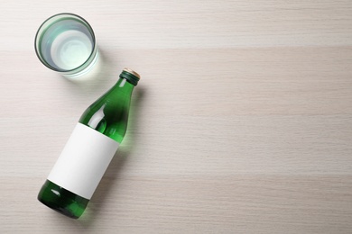 Bottle and glass with water on wooden table, flat lay. Space for text