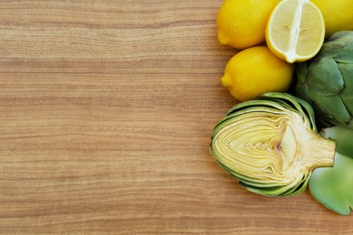 Photo of Artichokes and lemons on wooden table, flat lay. Space for text