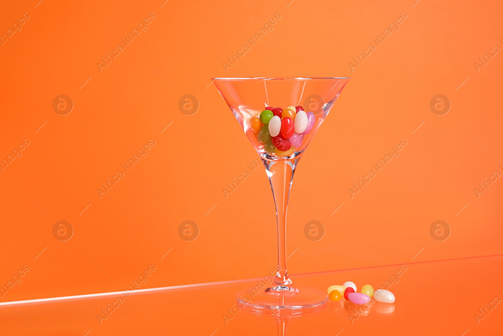 Photo of Martini glass with many tasty colorful candies on table against orange background